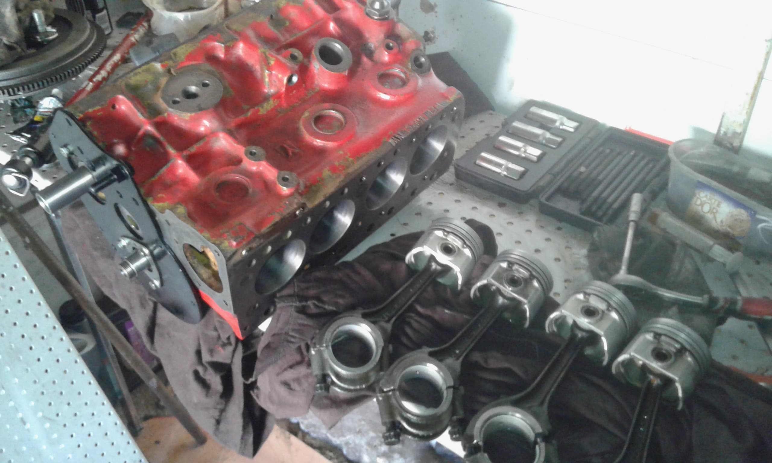 Rozebrany blok silnika po lewej na stole, po prawej cztery tłoki z korbowodami