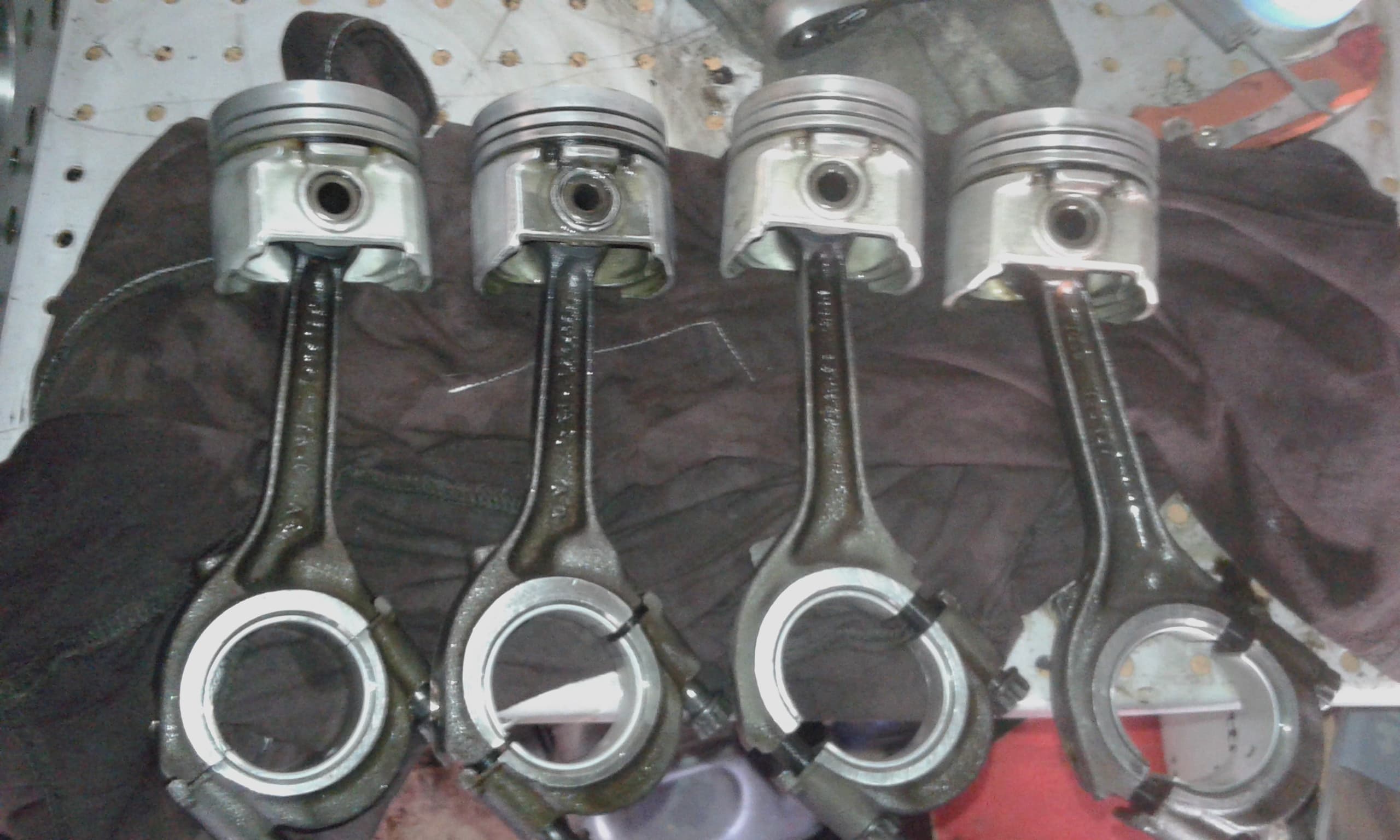 Widok na cztery tłoki wraz z korbowodami i panewkami, połozone jedne po drugim na stole