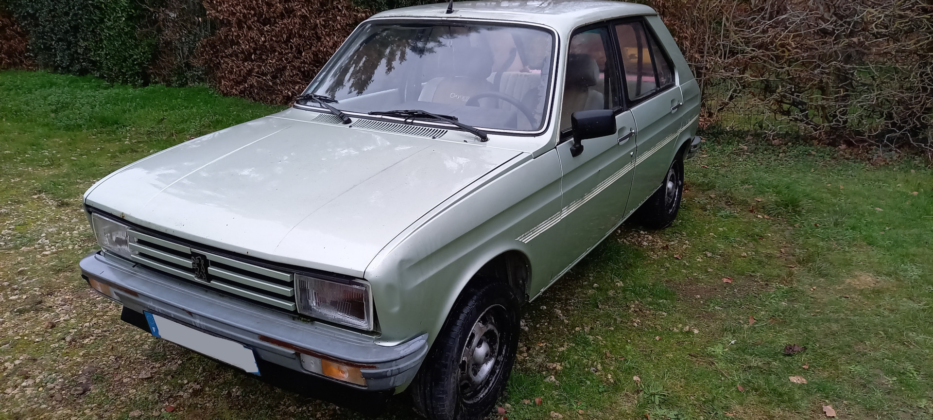 Zielony Peugeot 104 stojący na zewnątrz, zaniedbany przez lata. Widok od strony kierowcy
