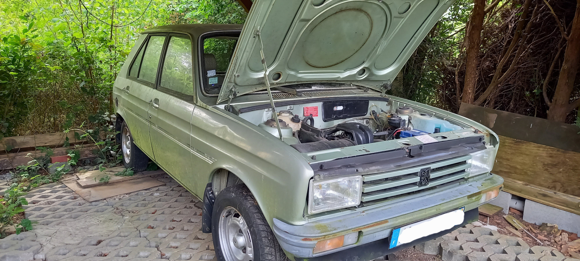 Widok 3/4 - Zielony Peugeot 104 pod wiatą z otwartą maską